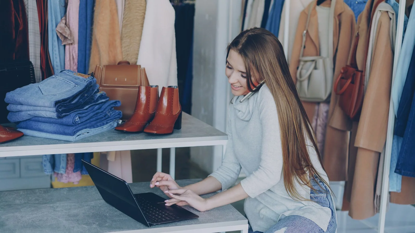 Inhaberin eines kleinen Ladengeschäfts kümmert sich am Laptop um ihr Unternehmen, während sie mit einer Kundin telefoniert