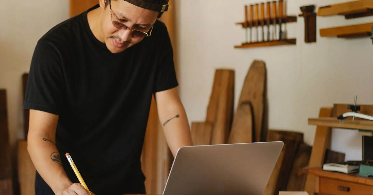 Handwerker notiert sich Informationen am Laptop in der Werkstatt