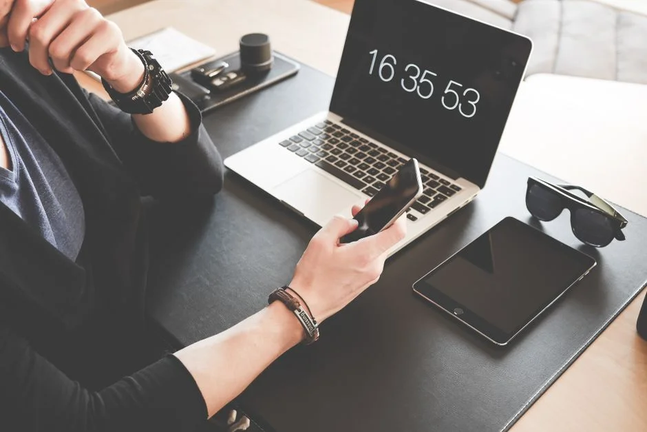 Person hält ein Smartphone neben einem geöffneten Laptop und Tablet.