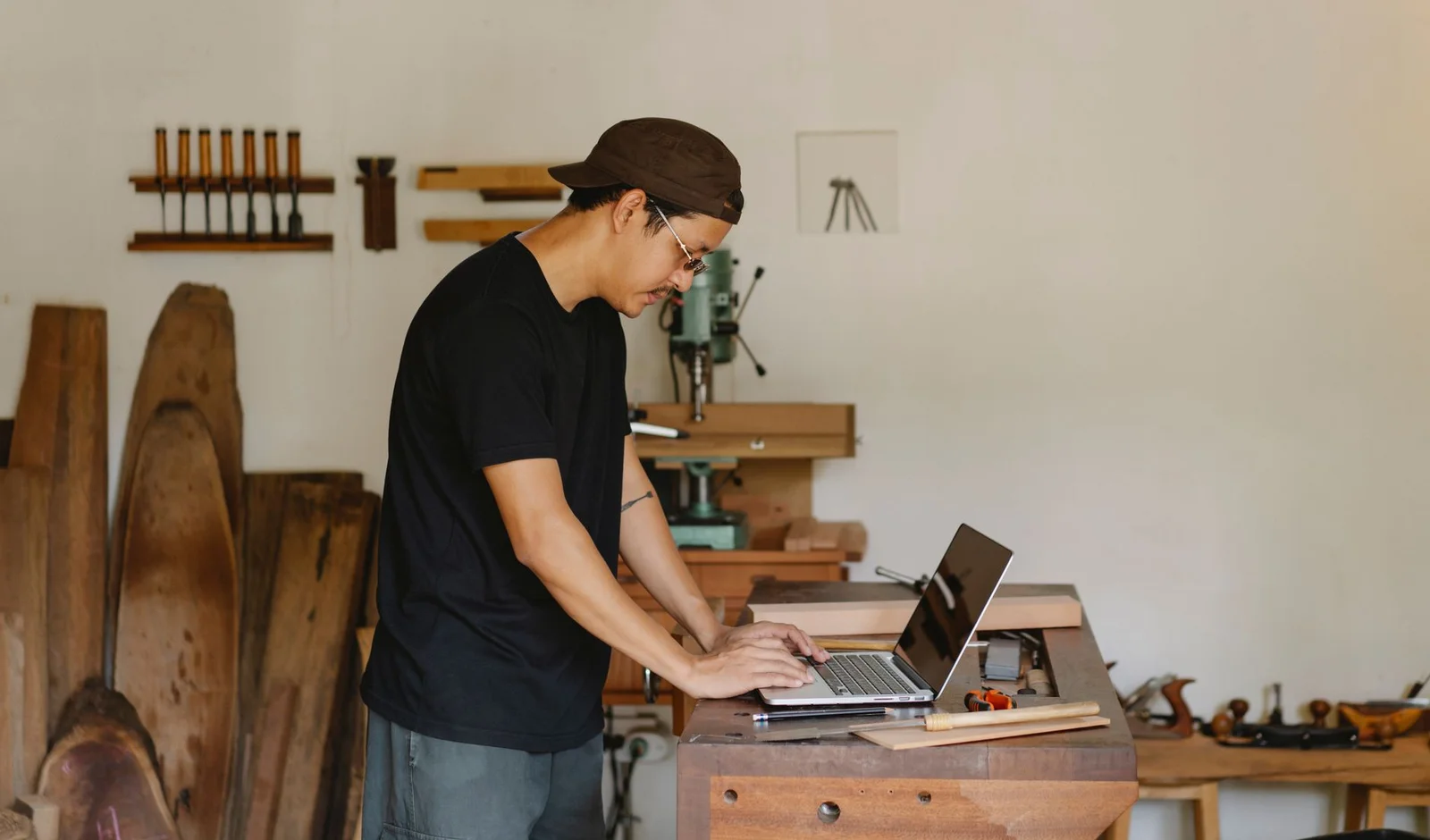 Handwerker steht an der Werkbank seiner Tischlerei und tippt auf einem Laptop