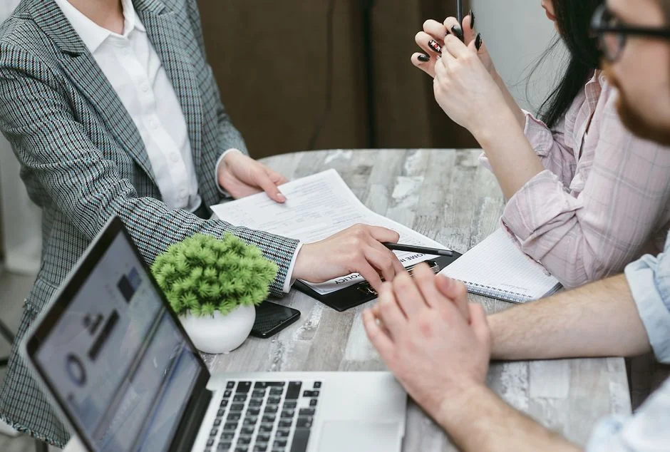 Drei Personen besprechen Unterlagen an einem Tisch mit Laptop