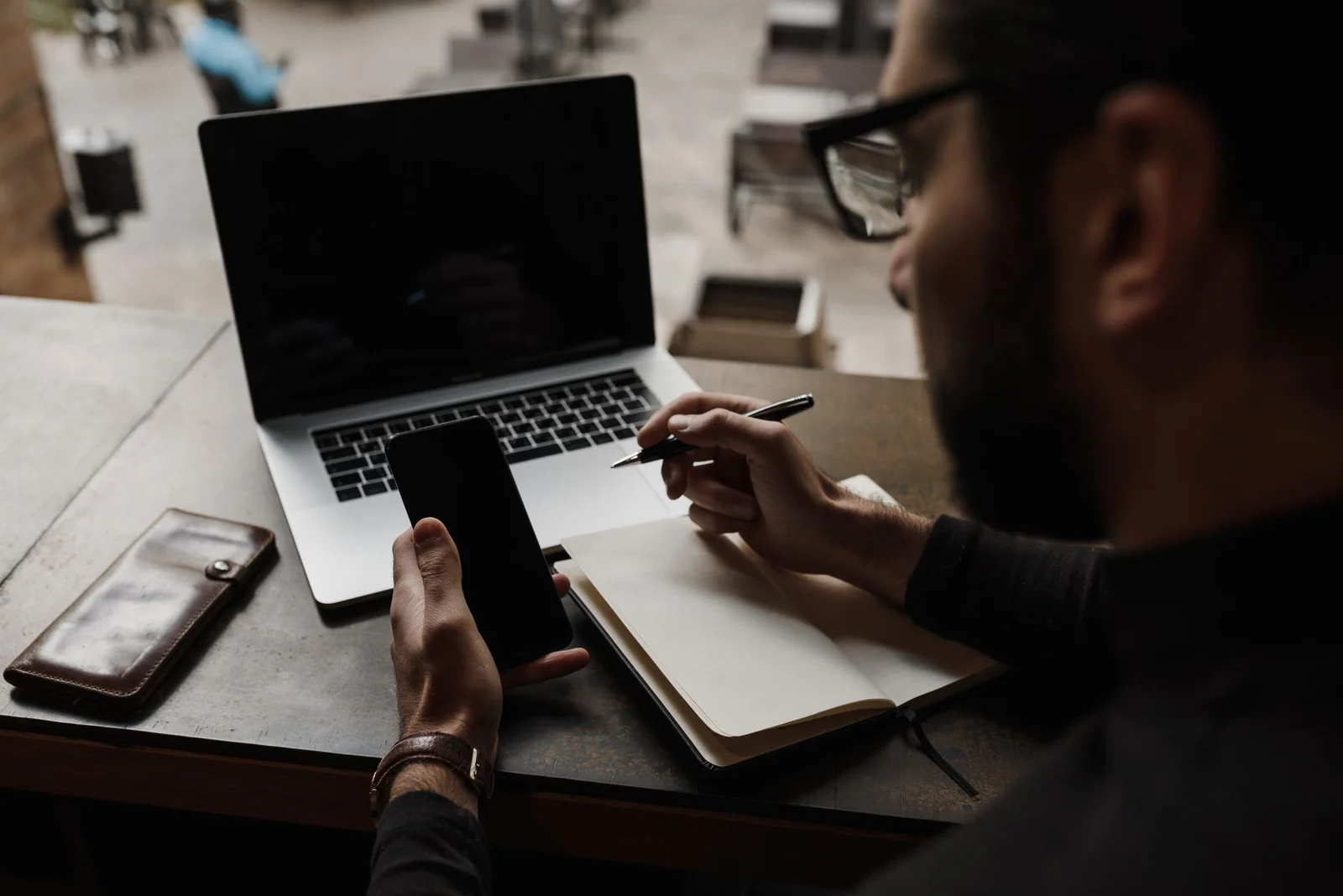 Unternehmer prüft eine Website auf dem Smartphone, daneben ein aufgeklappter Laptop am Arbeitsplatz