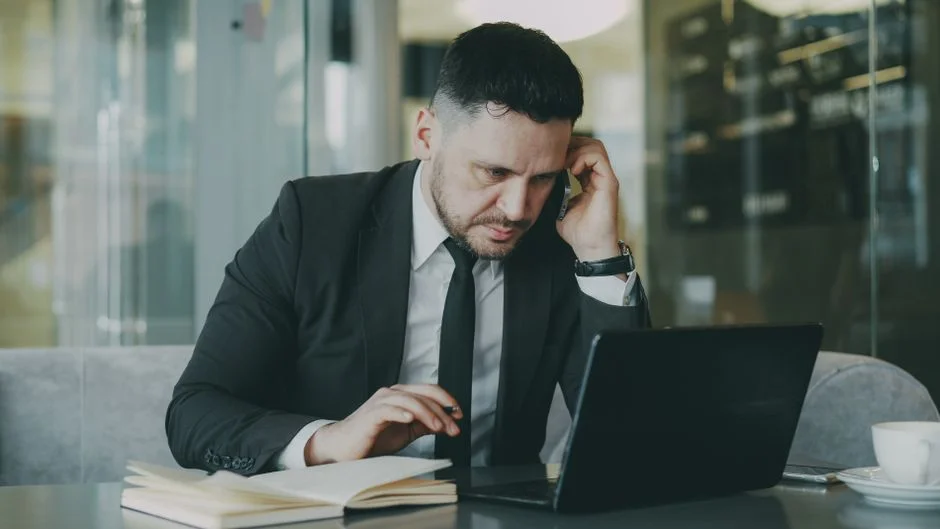 Mann telefoniert, während er an einem Laptop arbeitet.