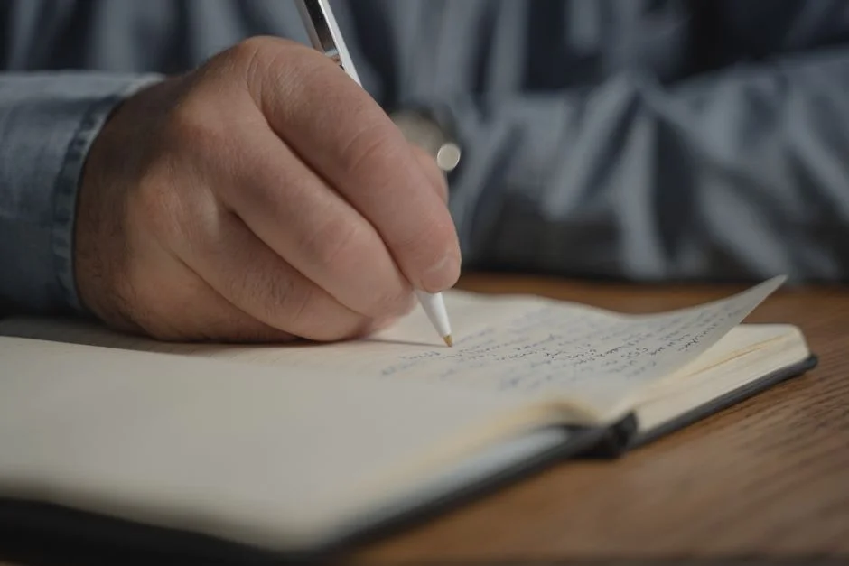Hand schreibt mit einem Stift handschriftliche Zeilen in ein aufgeschlagenes Notizbuch