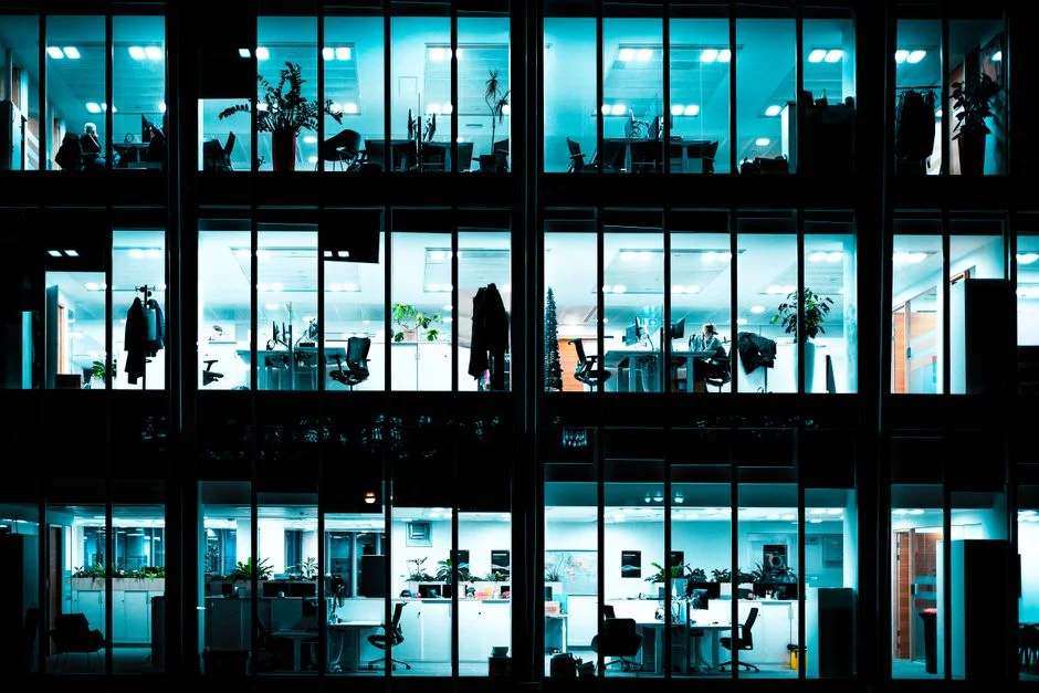 Beleuchtetes Bürogebäude mit sichtbaren Arbeitsplätzen bei Nacht