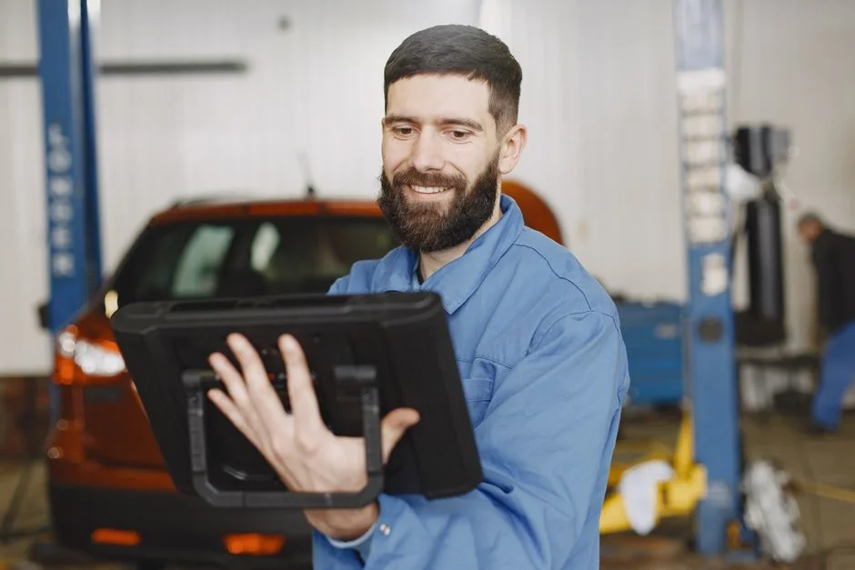 Kfz-Mechaniker mit Tablet vor einem Fahrzeug in der Werkstatt