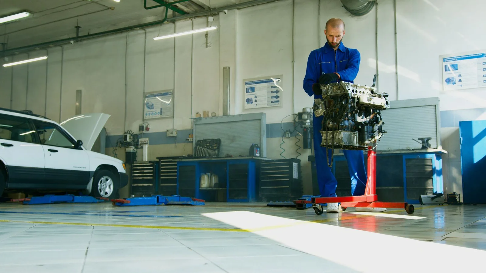 Mechaniker in blauer Arbeitskleidung bewegt einen Motor in einer hellen Kfz-Werkstatt