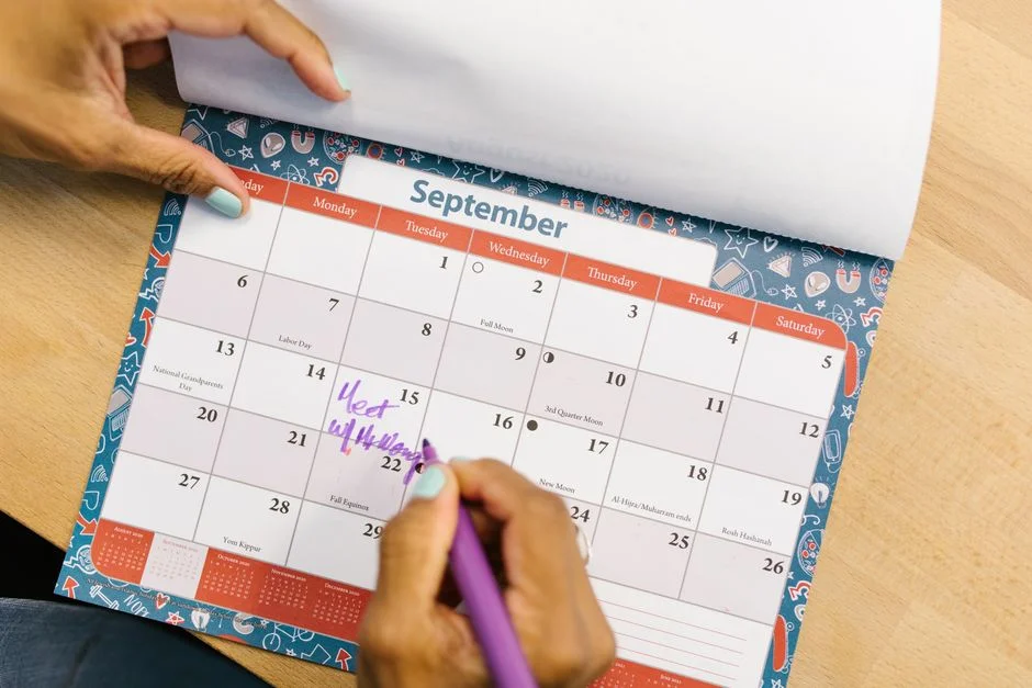 Hand trägt mit einem Stift einen Termin in einen aufgeschlagenen Monatskalender ein