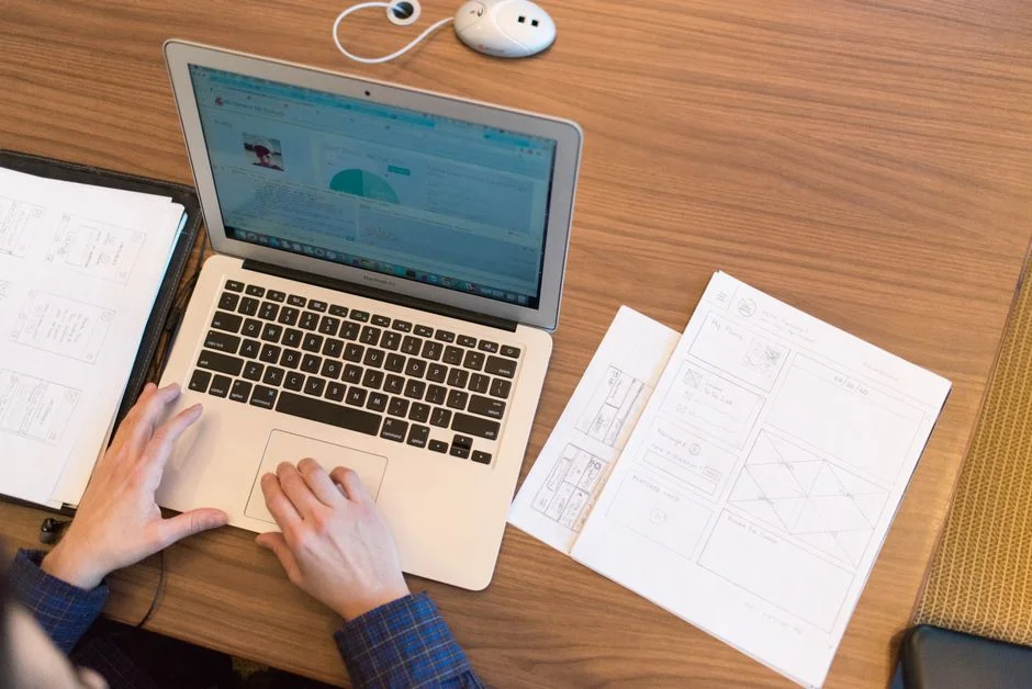 Hände arbeiten an einem Laptop neben Wireframes